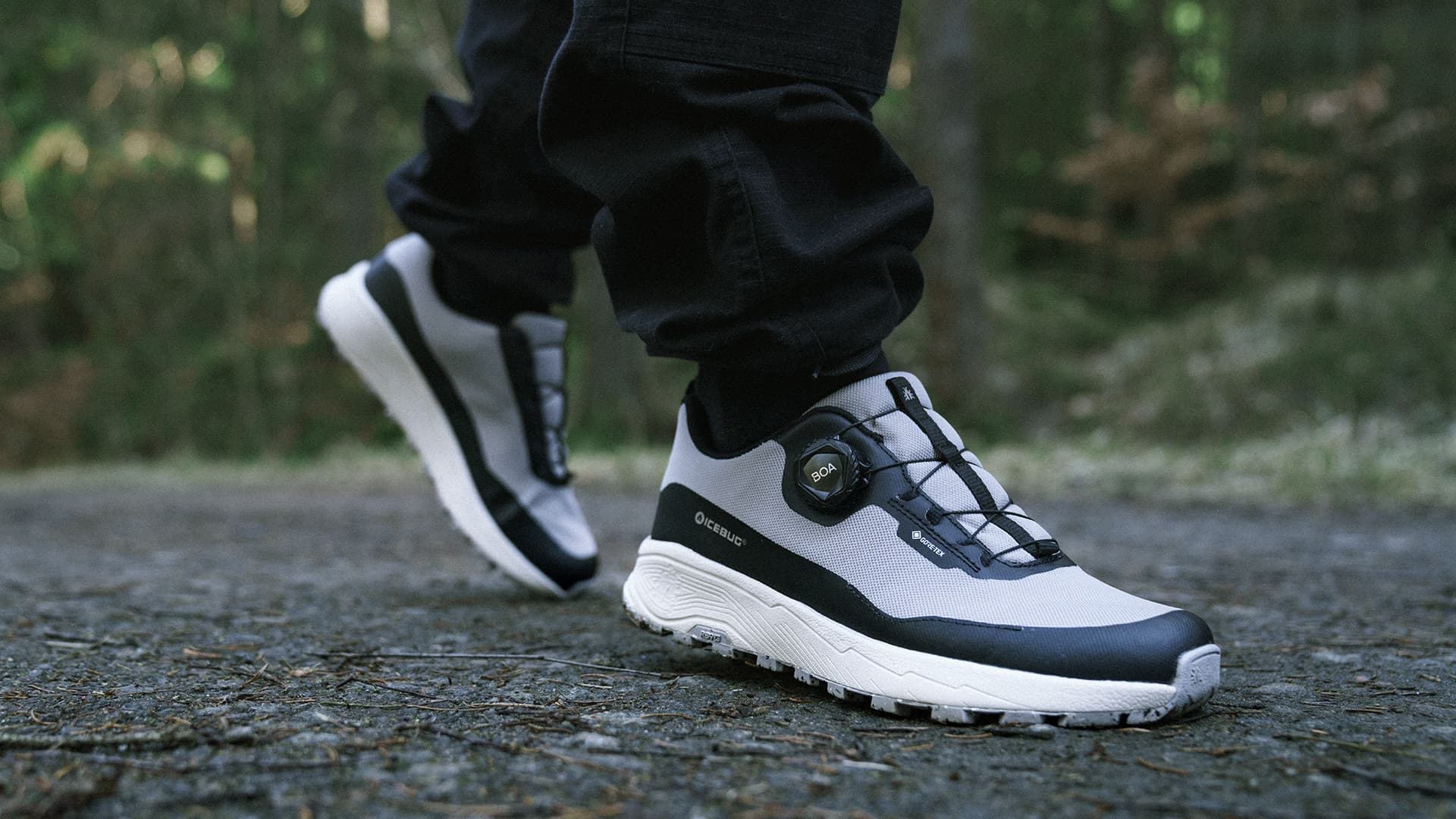 Person wearing black and white athletic shoes walking on a forest path, surrounded by greenery.