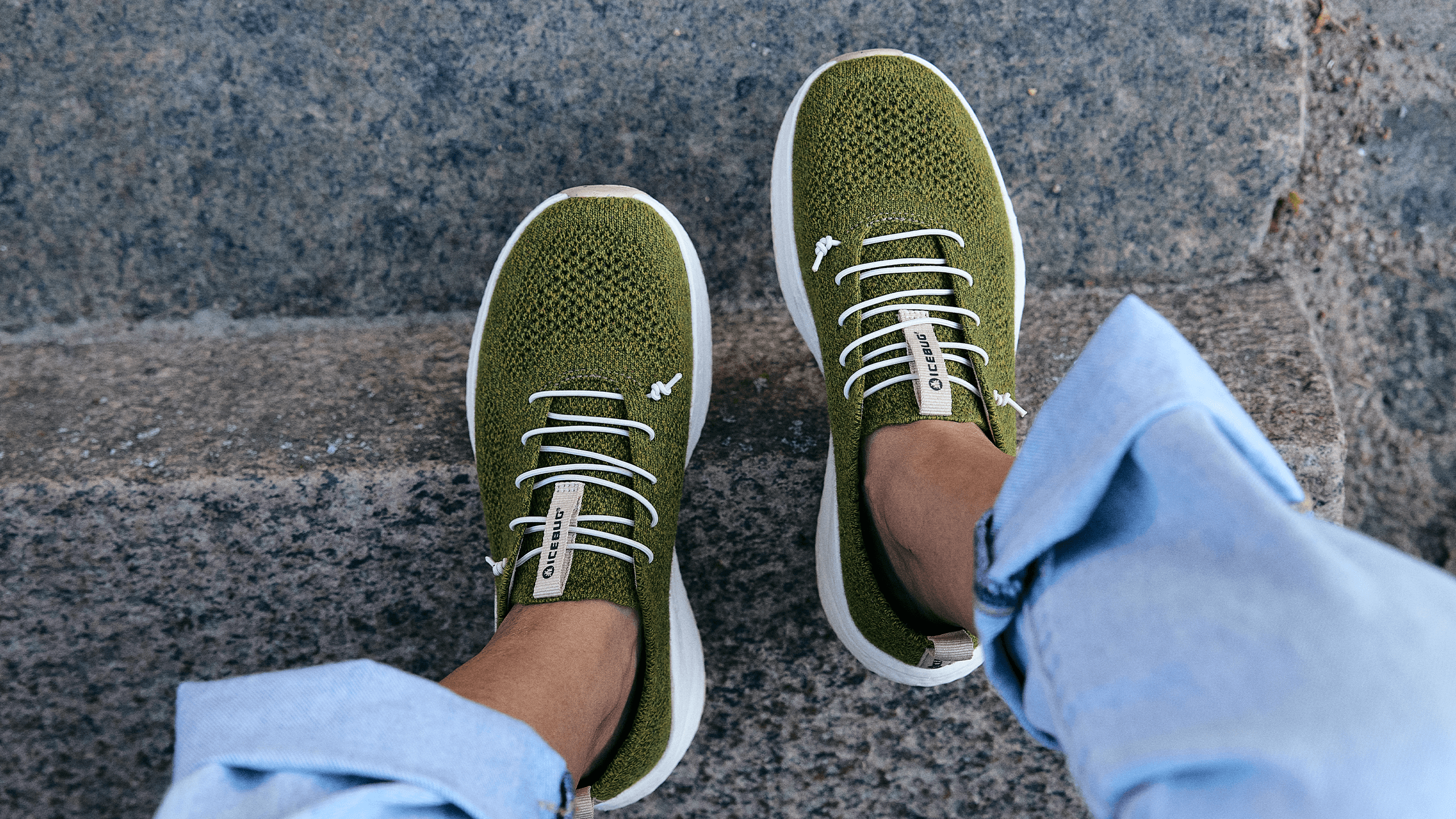 Person wearing green knit sneakers with white laces, standing on stone steps, wearing light blue jeans.